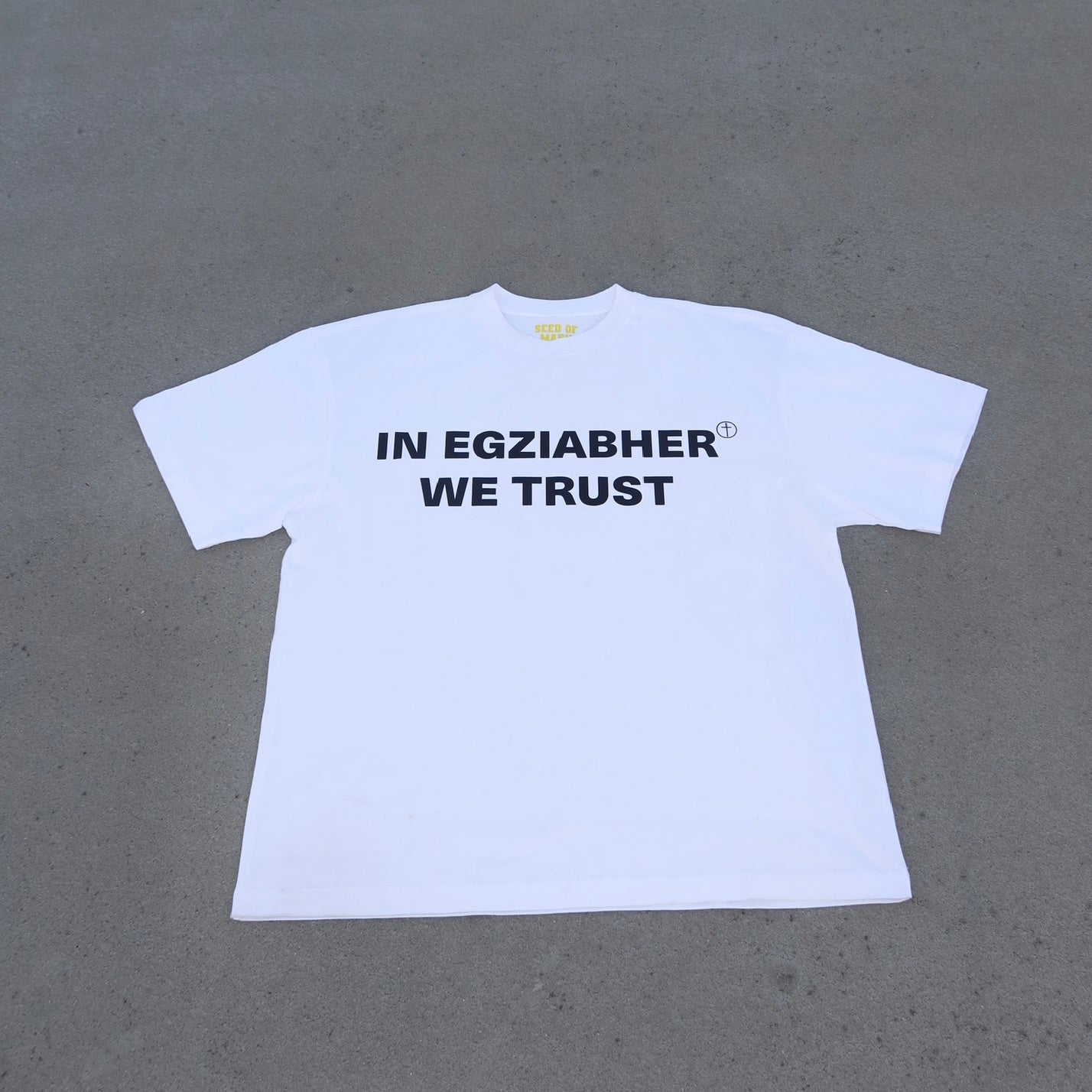 White t-shirt with 'IN EGZIABHER WE TRUST' text on a gray background
