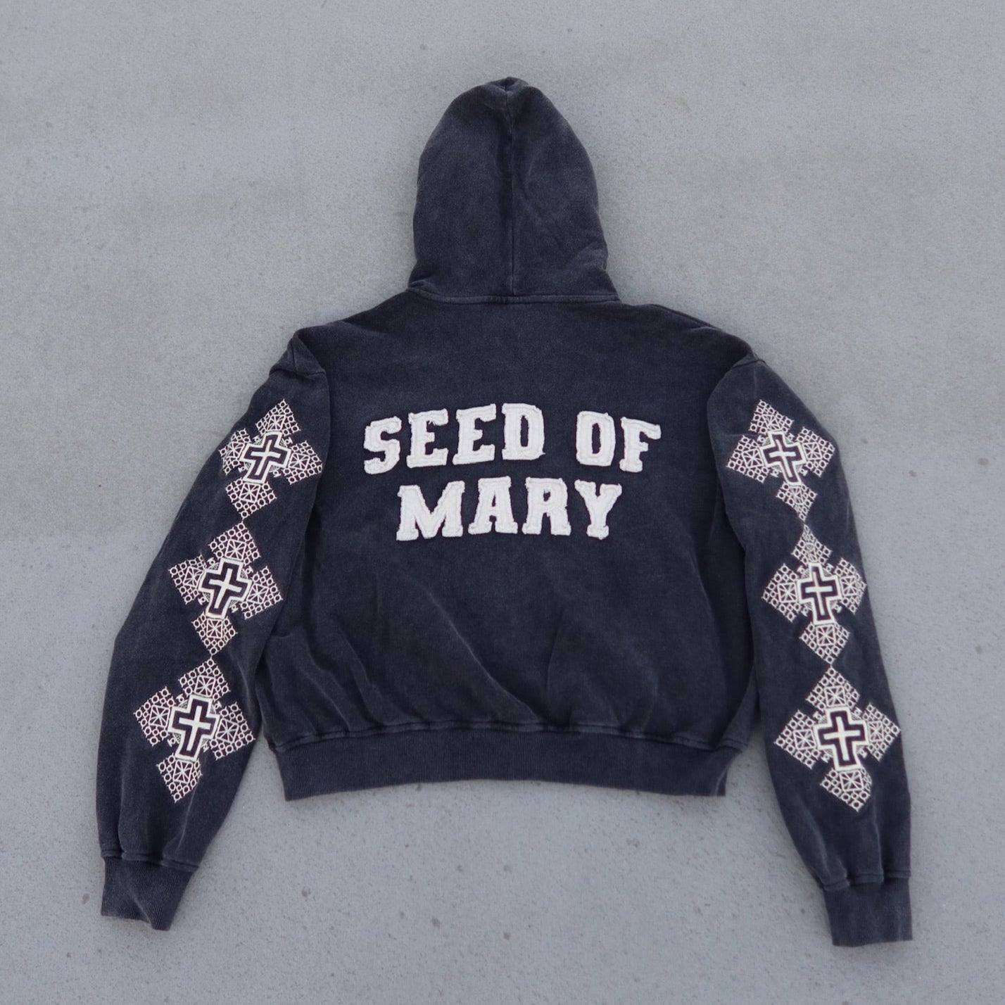 Black hoodie with 'SEED OF MARY' text on the back, displayed on a gray surface.